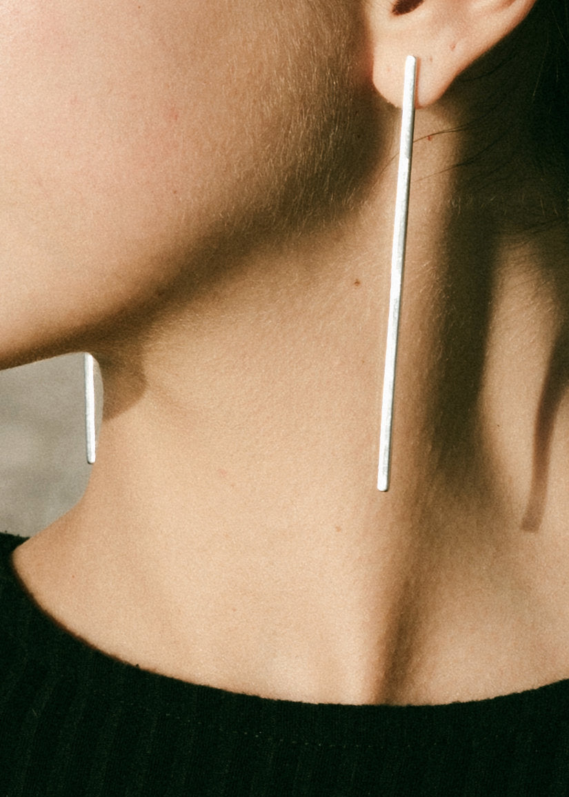 Close-up of a person wearing long, thin silver earrings.