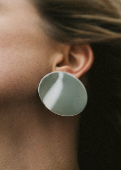 Close-up of a person wearing large round mirror-reflective earring with a neutral background