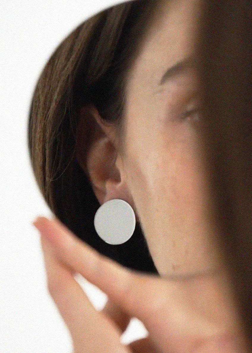 Close-up of a person wearing a round mirror reflective silver earring.