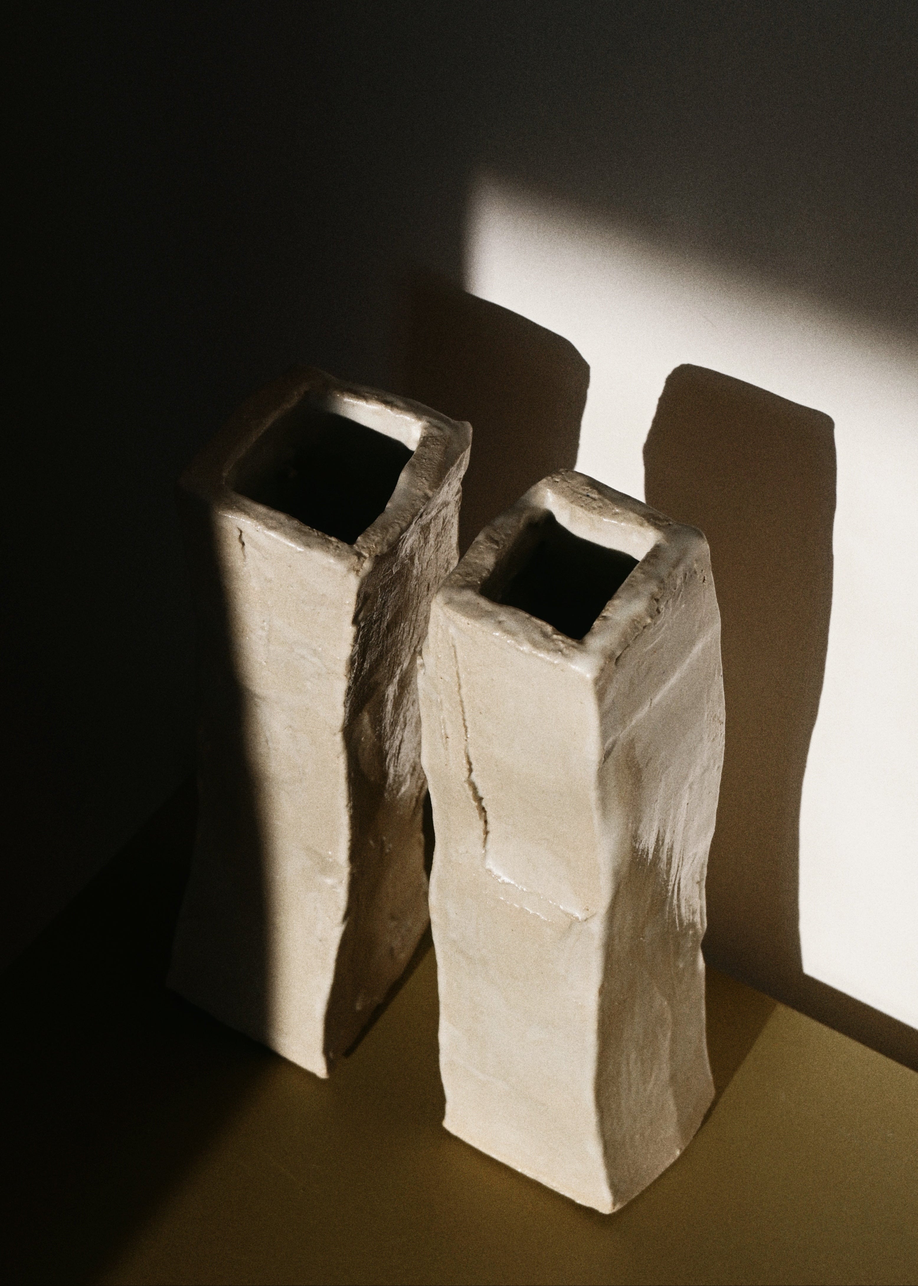 Two hand-carved ceramic vases casting shadows on a wall