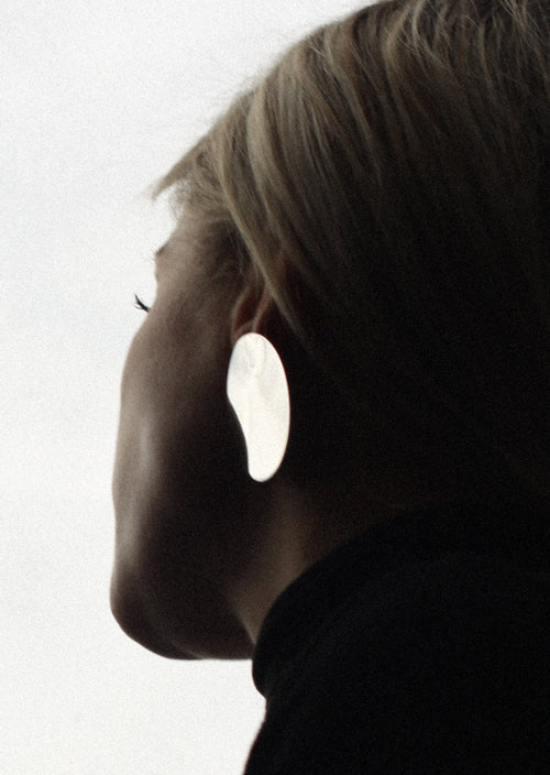 Close-up of a person wearing a large silver earring against a light background