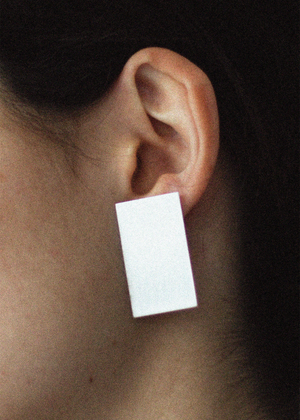 silver rectangular earring worn on an ear 