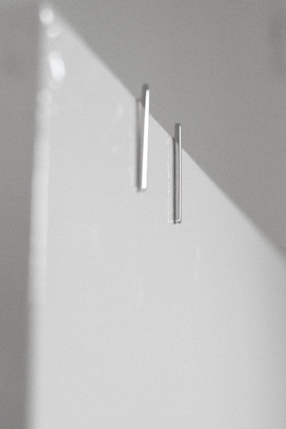 Two silver earrings on a white wall with soft shadows.