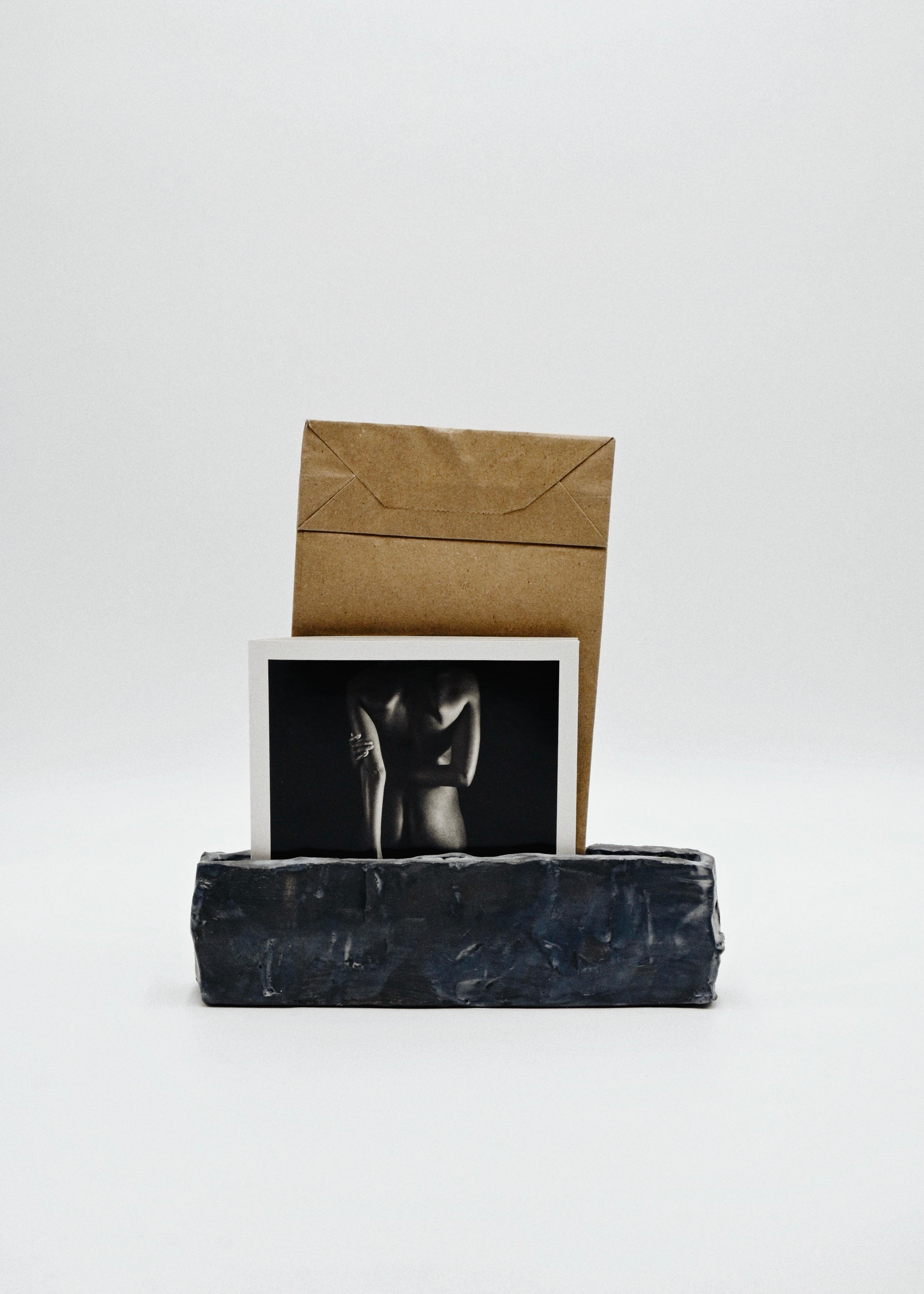 Black handcarved ceramic vessel with a photograph and brown envelope on a white background