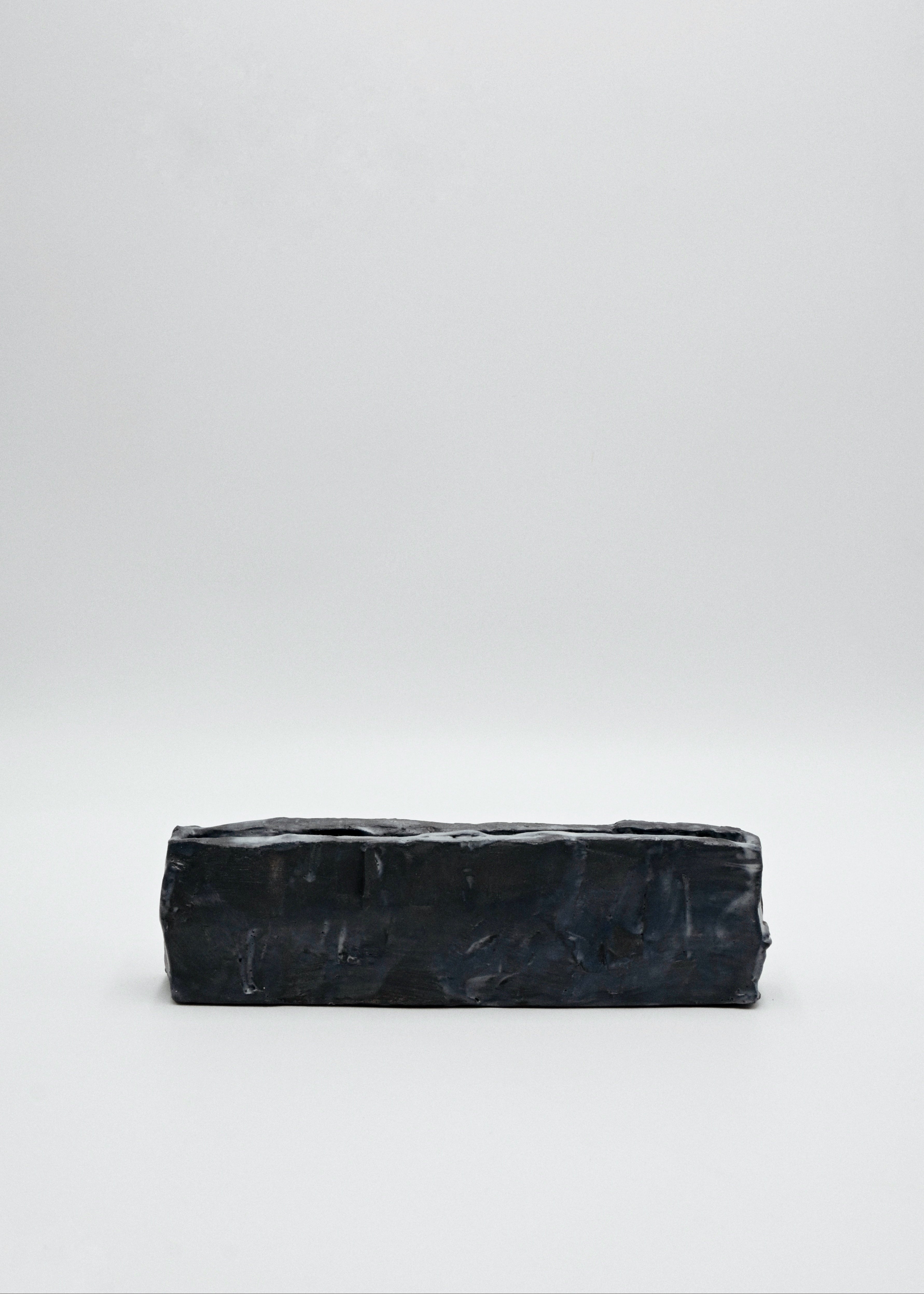 Black rectangular handcarved ceramic vessel on a white background
