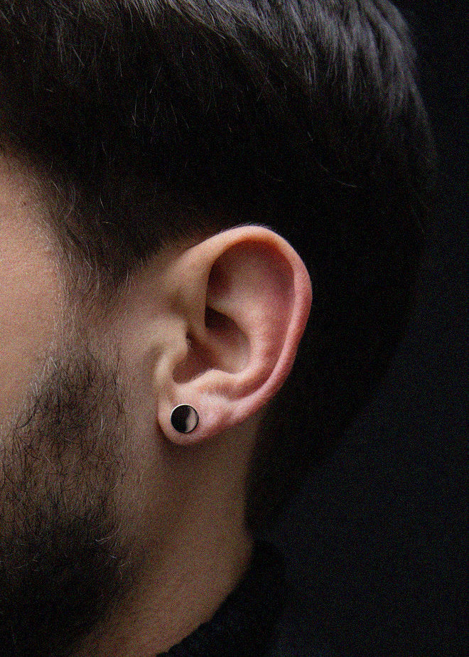 Close-up of an ear with a silver circular earring on a dark background