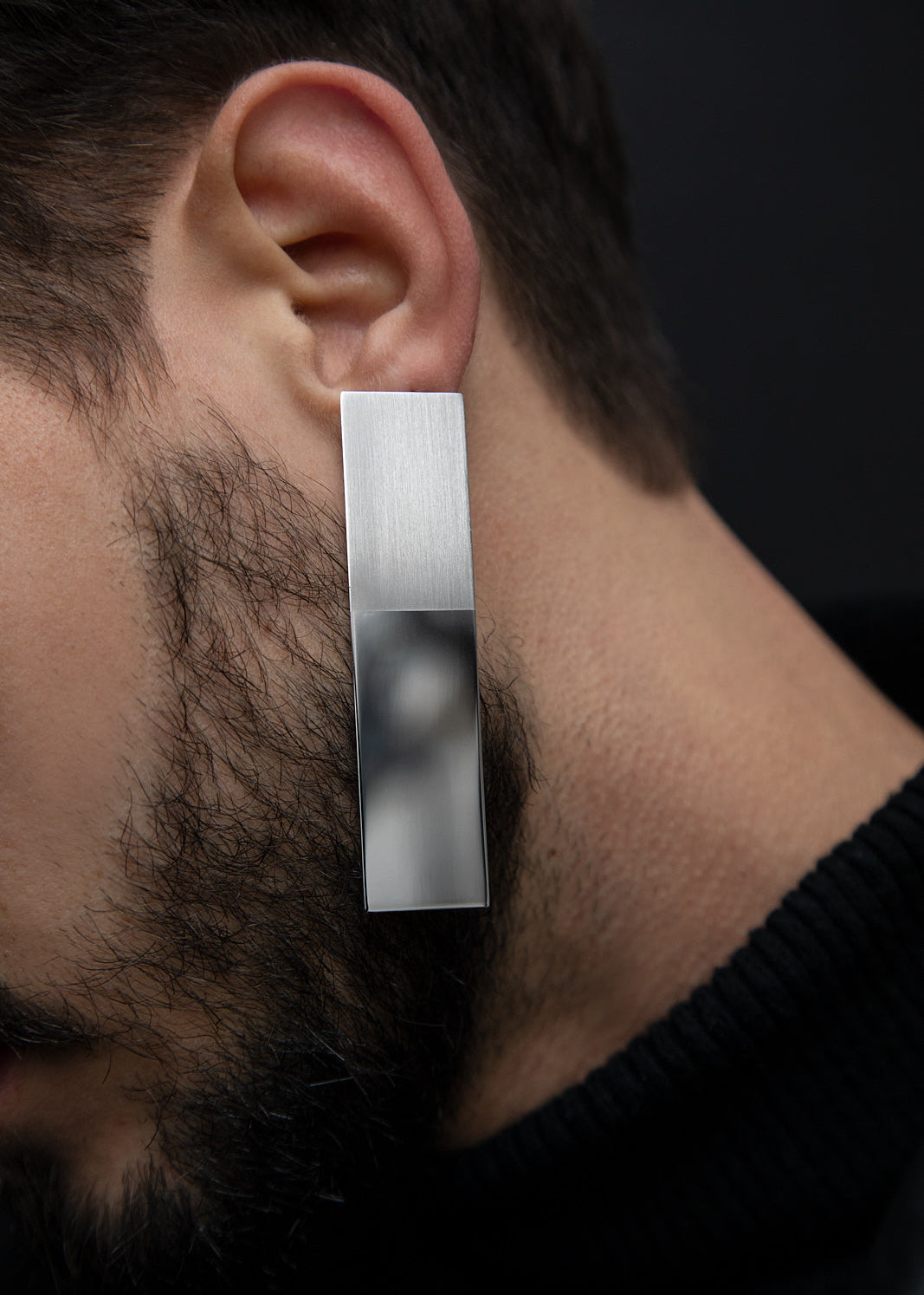 Big silver mirror reflective rectangular earring worn by a person with a dark background