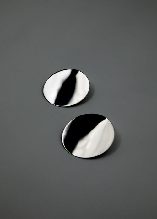 Two round, silver earrings mirror-polished on a gray background