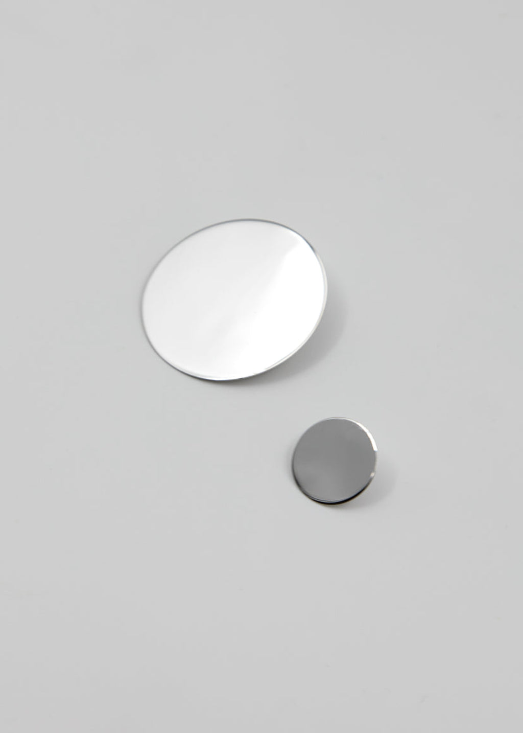 Two circular silver earrings on a gray background