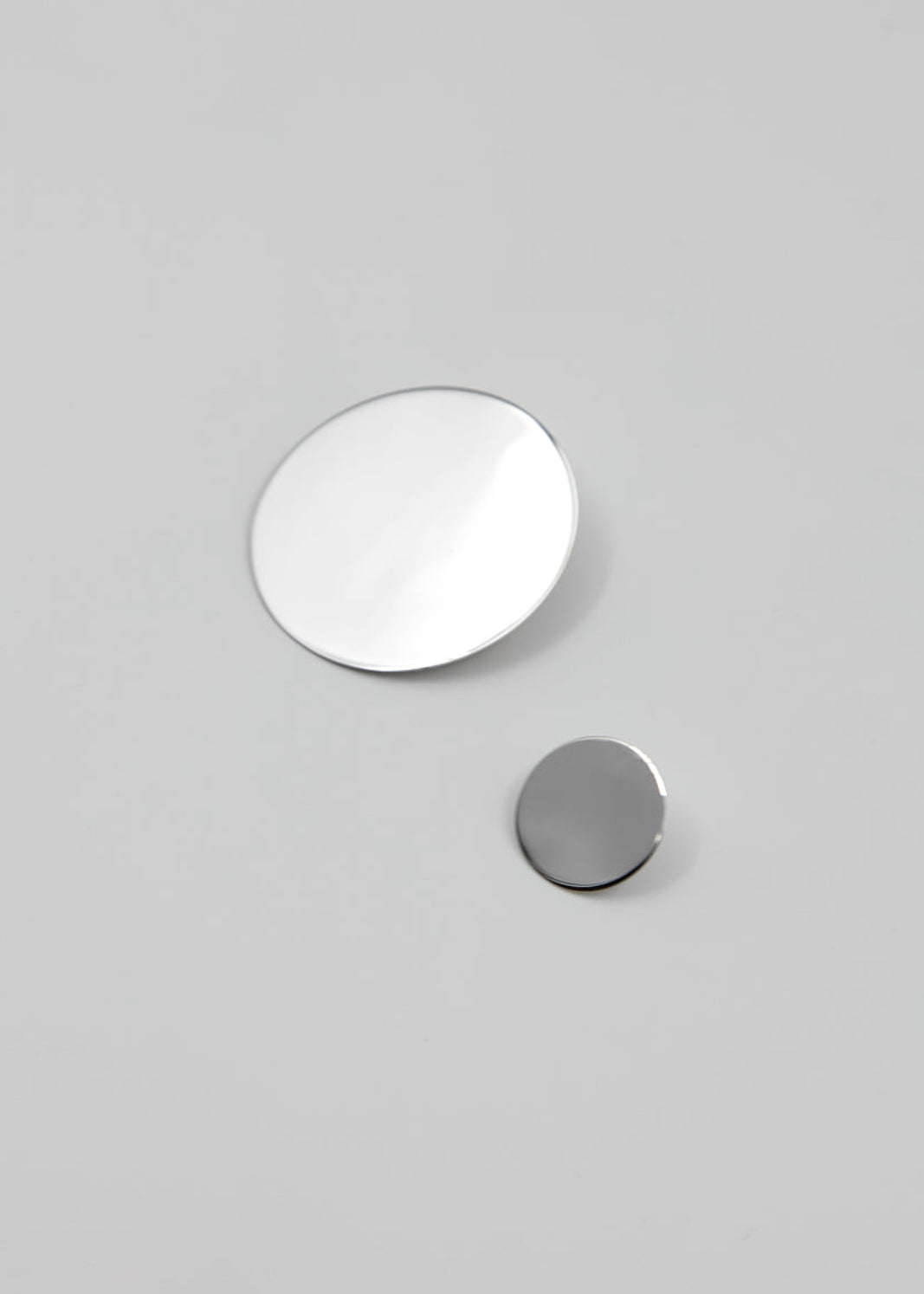 Two circular silver earrings on a gray background