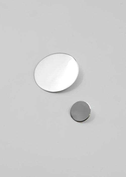 Two circular silver earrings on a gray background