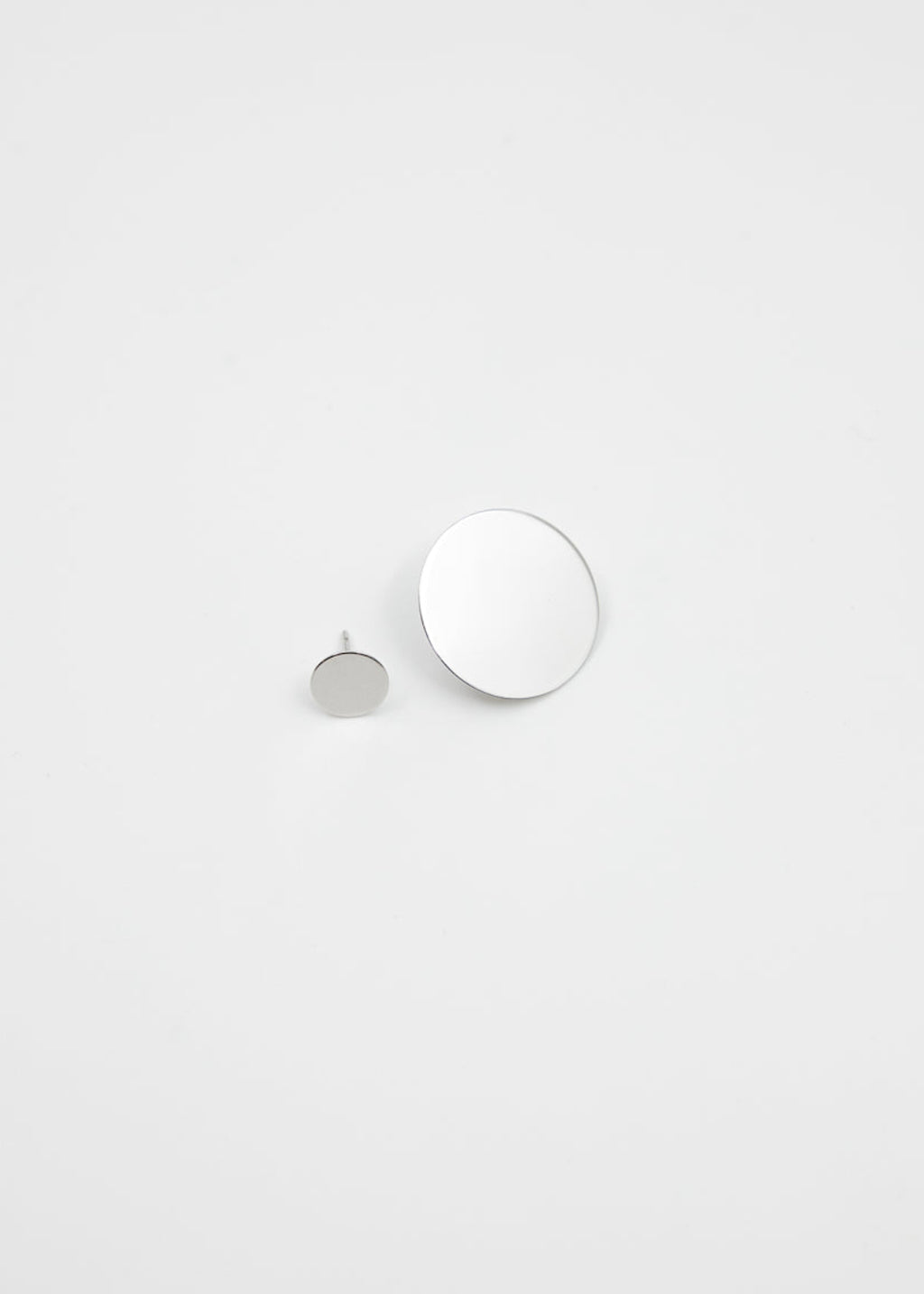 Two round mirror-polished silver earrings on a light gray background