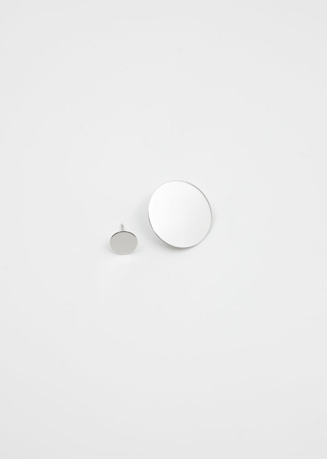 Two round mirror-polished silver earrings on a light gray background
