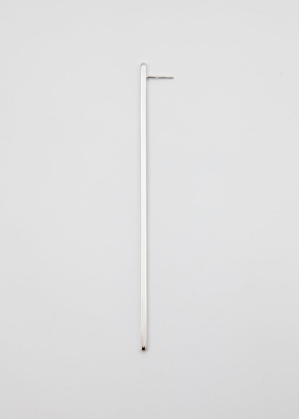 Long thin silver earring on a light gray background