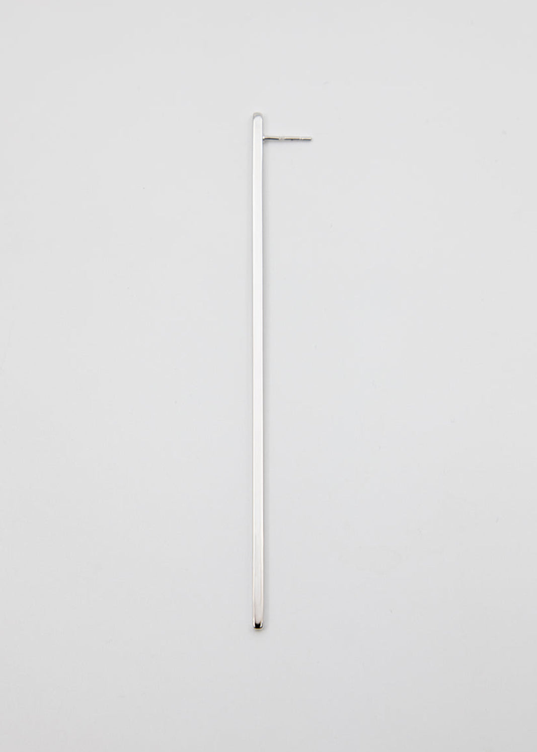 Long thin silver earring on a light gray background
