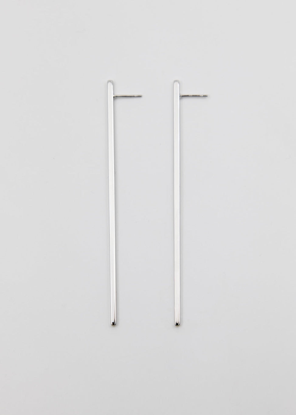 Two linear silver earrings on a light gray background
