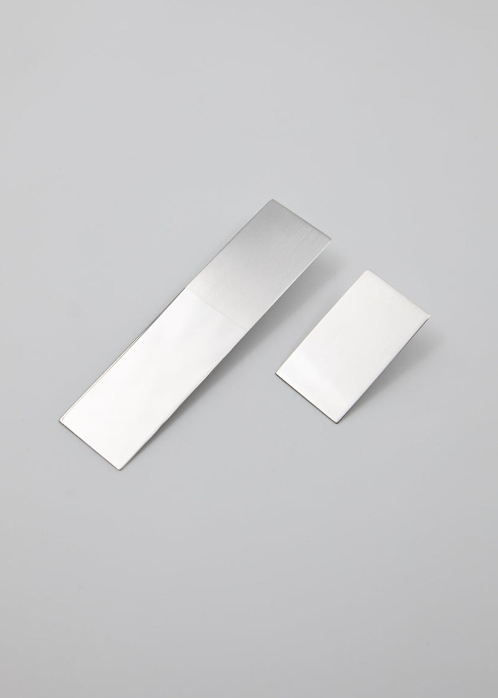 Two rectangular metallic earrings in different lengths on a gray background