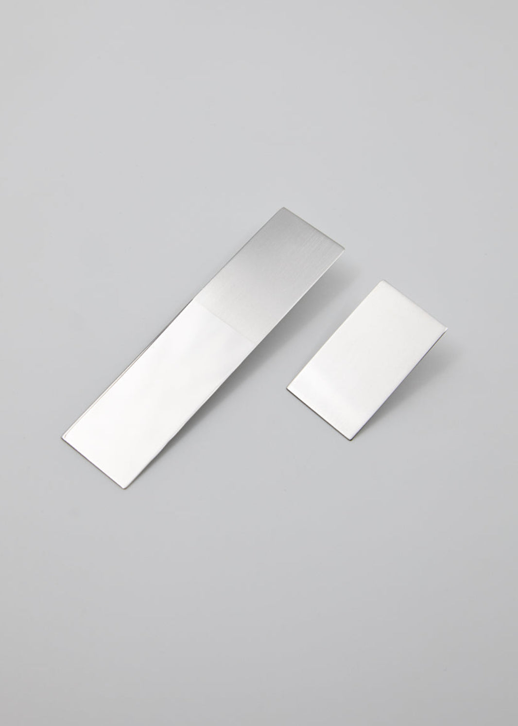 Two rectangular metallic earrings in different lengths on a gray background
