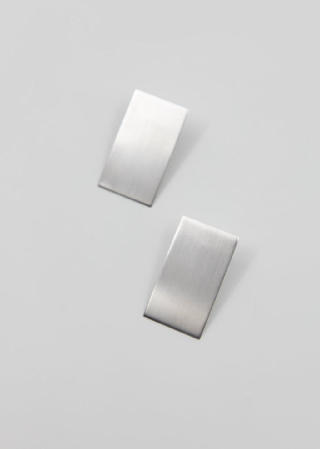 Two silver rectangular earrings on a light gray background