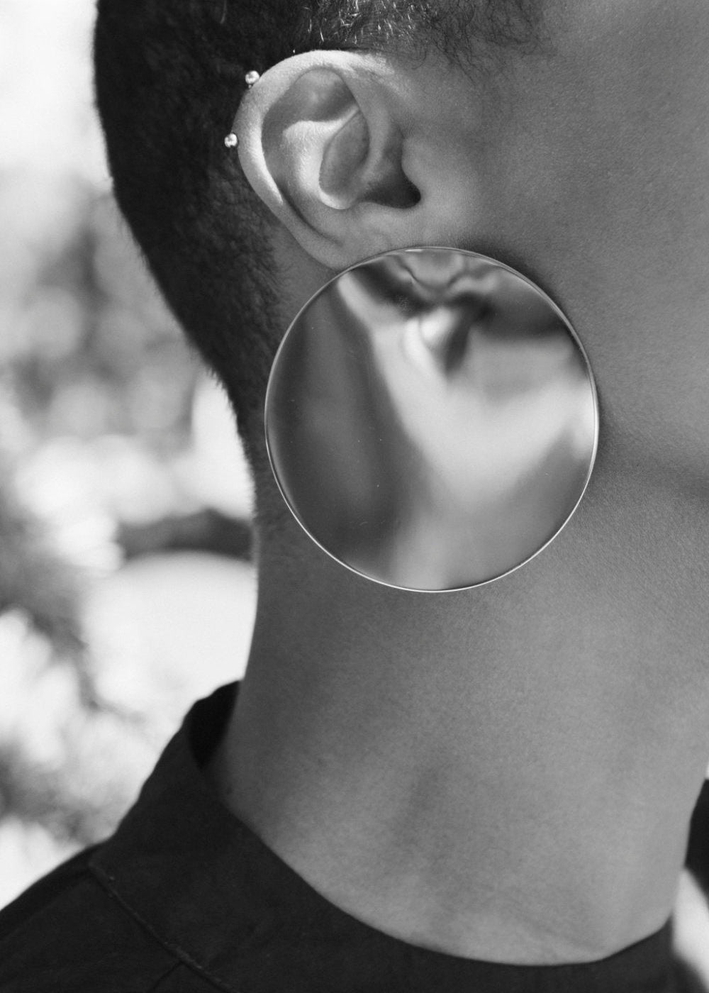 Close-up of a person wearing a very large round silver earring with a blurred natural background