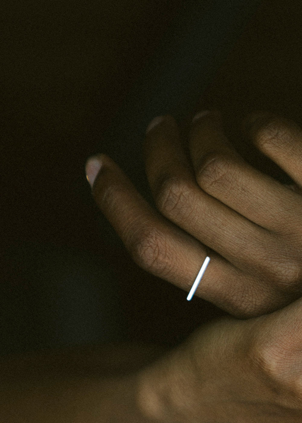Close-up of a hand with a thin linear silver ring on a dark background